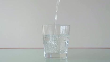 Pouring-water-in-short-glass-on-table-with-relfection,-still-close-up-shot-in-minimalist-setup