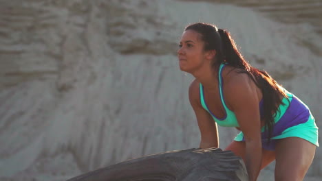 girl on a sand quarry pushing a wheel in training crossfit workout at sunset in the sun