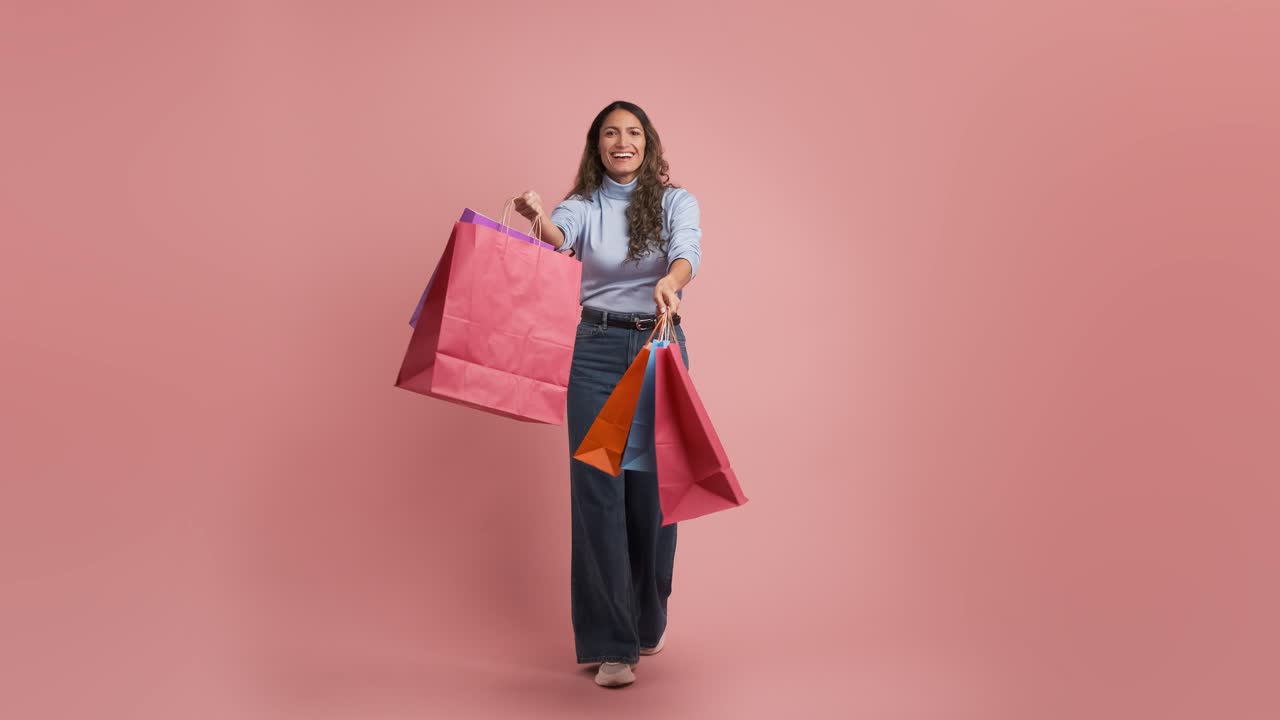 Full body adult colombian woman 30s dancing with shopping bags on pink background