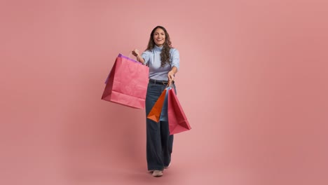 full body adult colombian woman 30s dancing with shopping bags on pink background