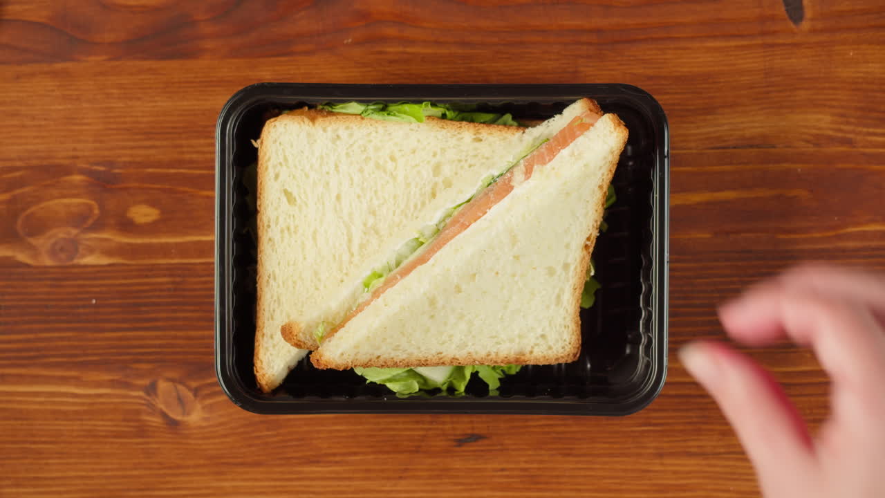 Mani che mettono un panino al salmone in un contenitore di plastica su un tavolo di legno
