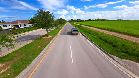 fpv drone following the futuristic tesla cybertruck riding by the highway. cyberpunk style auto in the countryside.