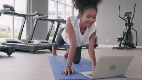 attractive, fit young black woman doing exercise yoga in gym. african american female loook at laptop lesson practicing yaga plank pose on social online internet class. healthy lifestyle concept