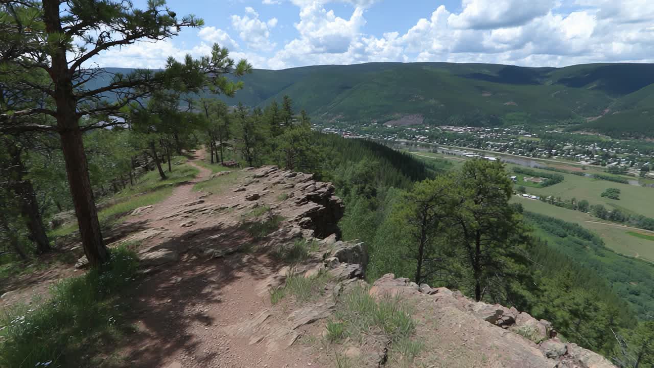 Breathtaking View Overlooking the Scenic Valley, Showcasing Lush Greenery, Rolling Hills, and Rocky Terrain Under a Brilliantly Blue Sky with Fluffy Clouds