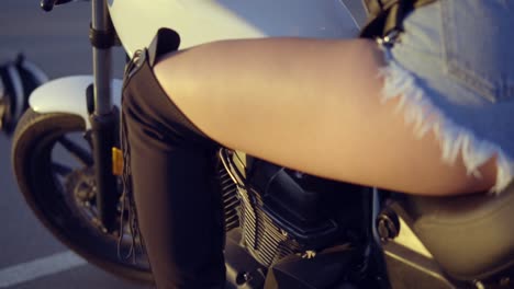 vista posterior de una motociclista femenina en pantalones cortos sentada en el asiento de la motocicleta. cerca de la joven mujer rizada en el helicóptero con su pierna