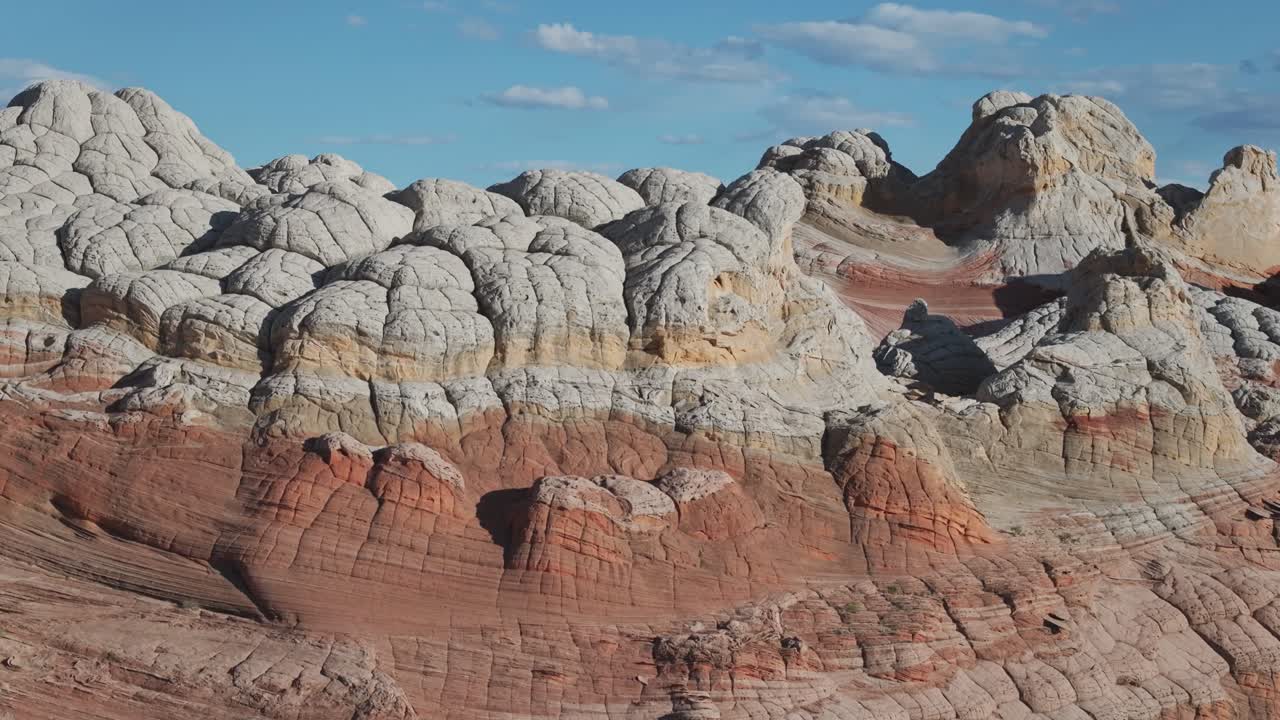 A drone raising altitude to reveal the unique sandstone rock features of White Pocket Arizona at midday surrounded by sandy desert