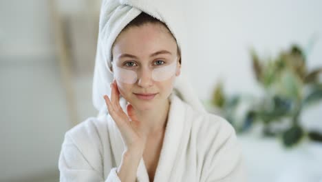 Retrato-De-Una-Mujer-En-Casa-Con-Una-Bata-De-Baño,-Una-Toalla-Y-Parches-Debajo-De-Los-Ojos