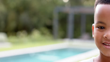 portrait of happy african american boy smiling in garden by pool, copy space, in slow motion