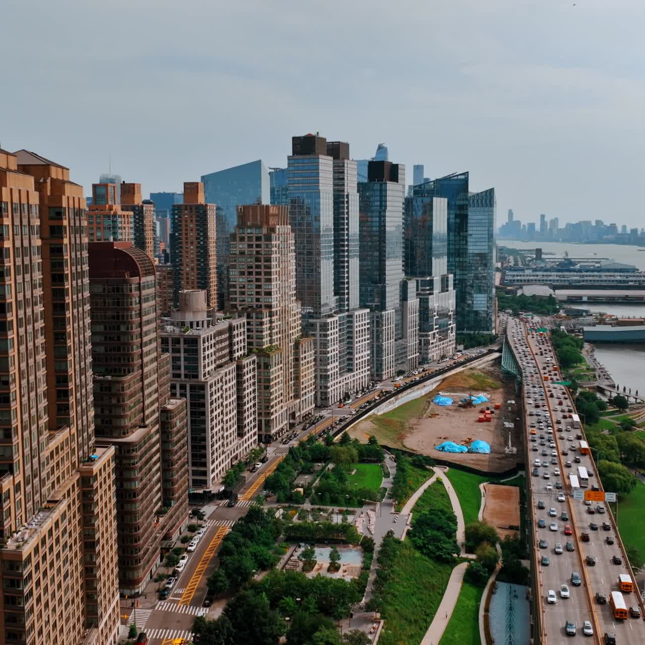 Flying along the green area at Hudson waterfront. Busy highway full of cars at daytime. Top view