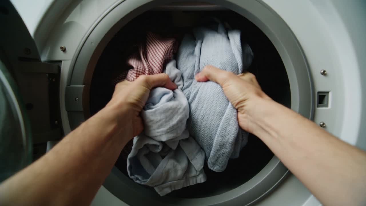 Approaching frontload washer, hands opening door in laundry corner, pulling wet clothes for drying