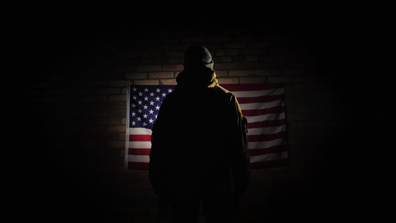 la silueta de un hombre -- mira la bandera americana en la pared de ladrillos la vista desde atrás