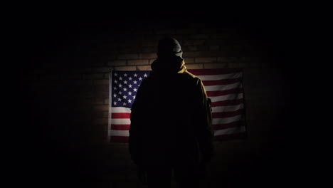 The-Silhouette-Of-A-Man----He-Looks-At-The-American-Flag-On-The-Brick-Wall-The-View-From-Behind