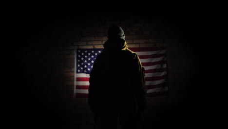 the silhouette of a man -- he looks at the american flag on the brick wall the view from behind