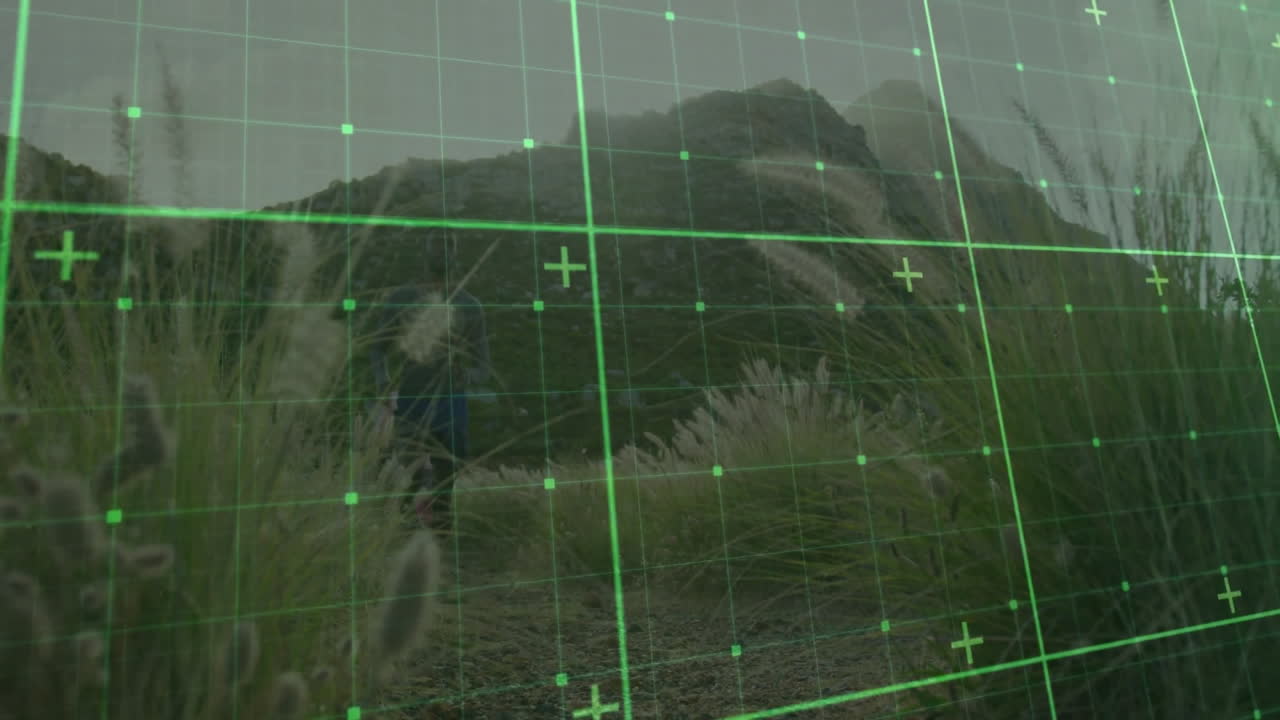 Two hikers exploring mountain trail among grasses, demonstrating technology via green digital grid