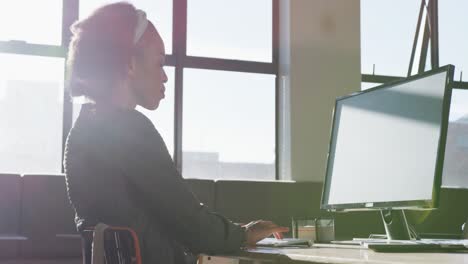 Mujer-De-Negocios-Afroamericana-Sentada-A-La-Mesa-Y-Usando-Una-Computadora-En-La-Oficina