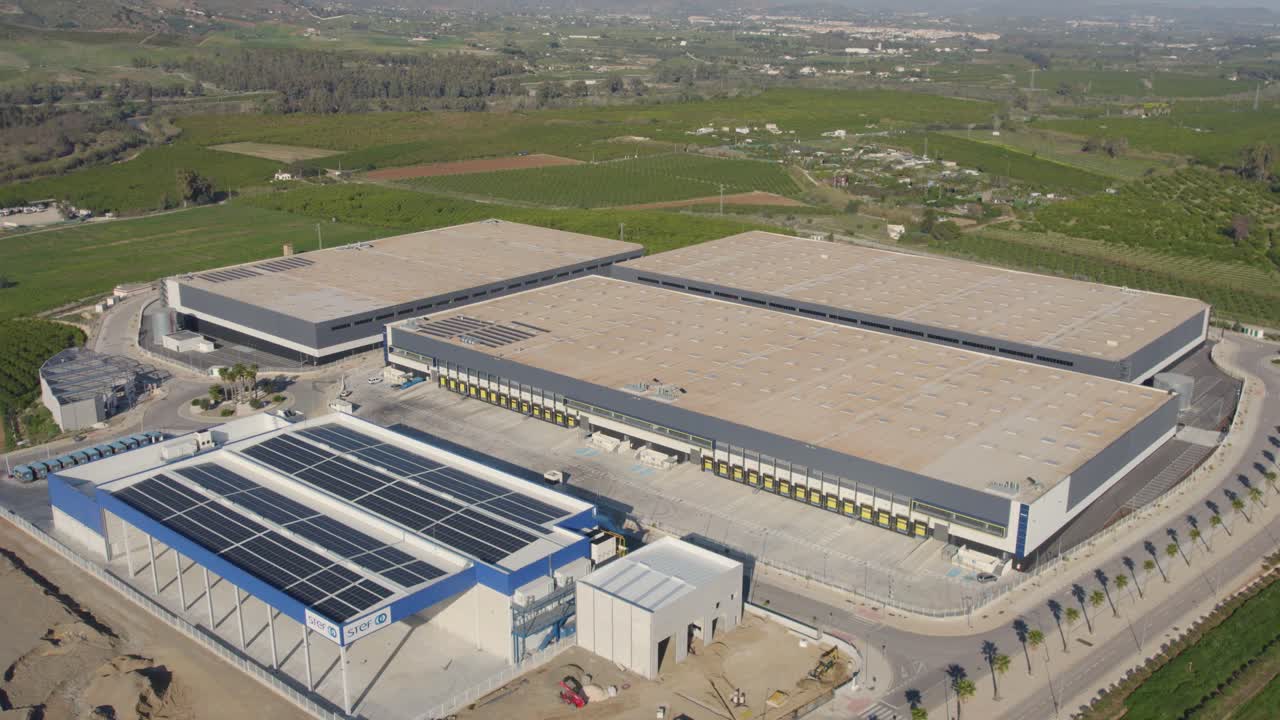 órbita aérea sobre una gran instalación de distribución de envío comercial industrial en las tierras de cultivo de cartama españa