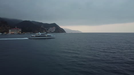 Moody-Sky-as-Santa-Catalina-Express-Ship-Departs-from-Avalon-Bay,-California,-Drone-Tracking-Shot