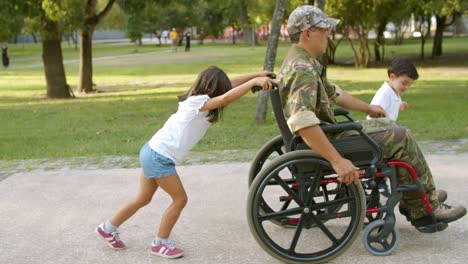 kinder, die einem behinderten militärvater helfen, einen schweren rollstuhl zu rollen