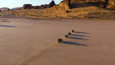 Aerial-view-around-a-convoy-of-cars,-golden-hour-in-the-deserts-of-Saudi-Arabia