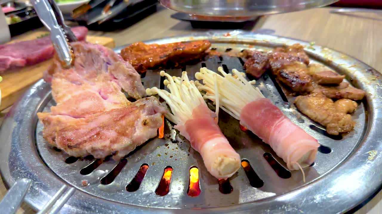 Close-up of Korean BBQ grilling meat and mushrooms on a tabletop grill in a Bangkok restaurant. Bright lighting enhances the vibrant colors