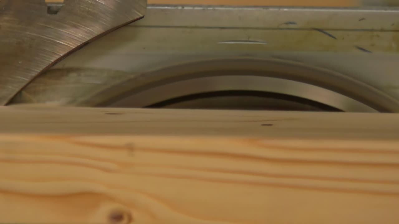 A close-up video captures a wooden block being cut through a high-speed rotating circular saw blade at a sawmill