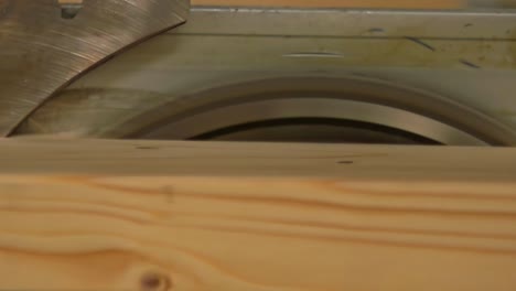 a close-up video captures a wooden block being cut through a high-speed rotating circular saw blade at a sawmill