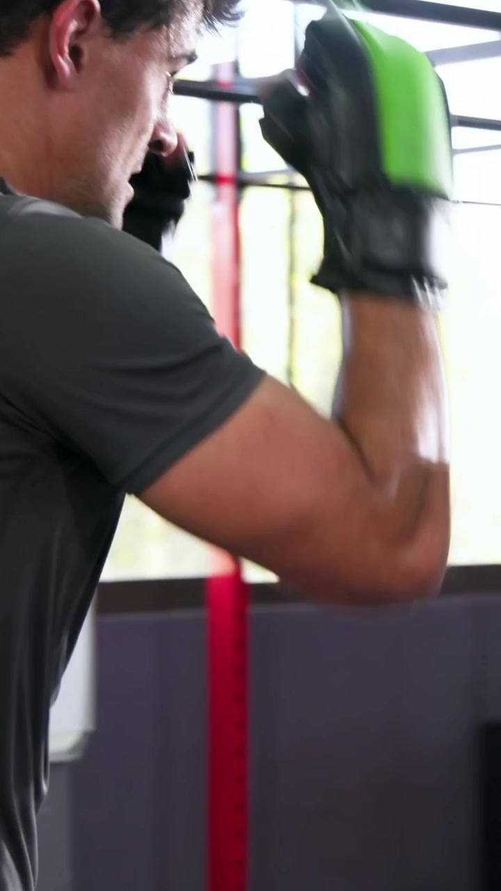 Vídeo vertical: Boxeador de luvas com camiseta cinza dando jabs em uma almofada amarela para treino.