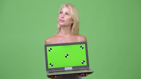 young happy beautiful businesswoman thinking while showing laptop