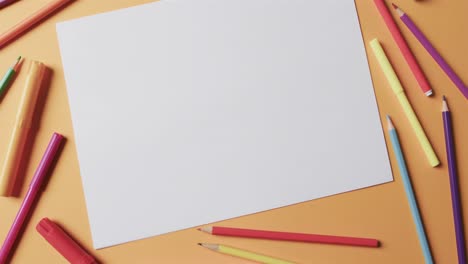 overhead view of blank sheet of paper with school stationery on beige background, in slow motion