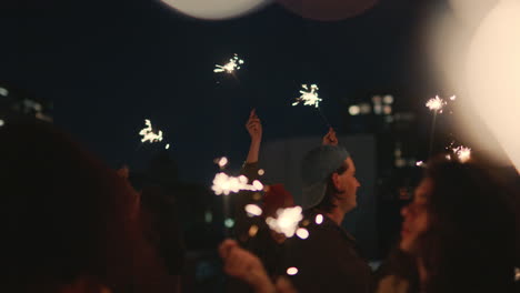 Fröhliche-Freunde-Halten-Wunderkerzen-In-Der-Hand-Und-Feiern-Silvester-Auf-Dem-Dach-Bei-Sonnenuntergang-Und-Haben-Spaß-Daran,-Die-Feiertagsfeier-Zu-Genießen