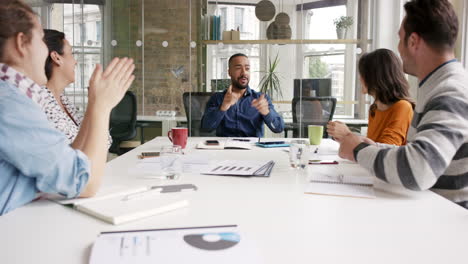 diverse business people clapping in creative team meeting celebrating success in casual modern office boardroom with natural light and large open windows