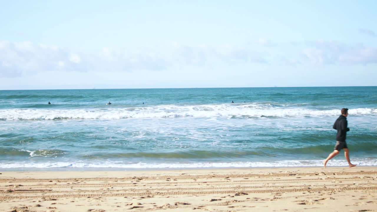 한 남자가 해변에서 조깅할 때 서퍼들은 파도를 잡기 위해 노를 젓는다