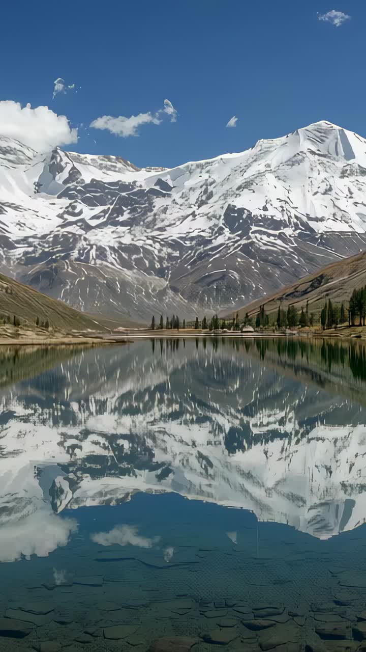 Vertical video: Reflecting snowy peaks shimmering in lake, cumulus drifting and ripples forming