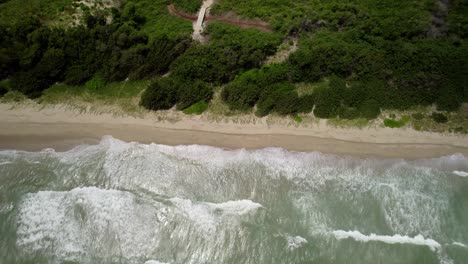 A secluded tropical beach with waves crashing onto the sandy shore, aerial view