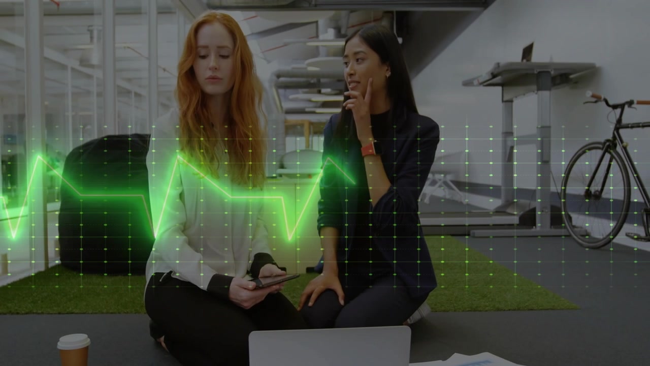 Due donne del team che esaminano i design su un laptop, con lo scorrimento del telefono che provoca un'onda verde pulsante.