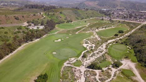 Stunning-Aerial-drone-footage-of-Beautiful-Golf-Course-with-lush-greens-and-fairways-with-players-playing-on-a-sunny-day-with-mountains-in-the-background