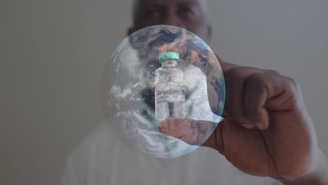 Spinning-globe-against-portrait-of-male-african-american-man-holding-covi-19-vaccine