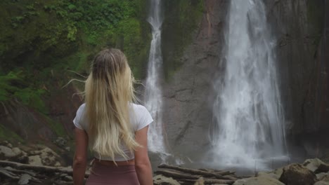 attractive blond woman watching powerful water flow of waterfall in canyon