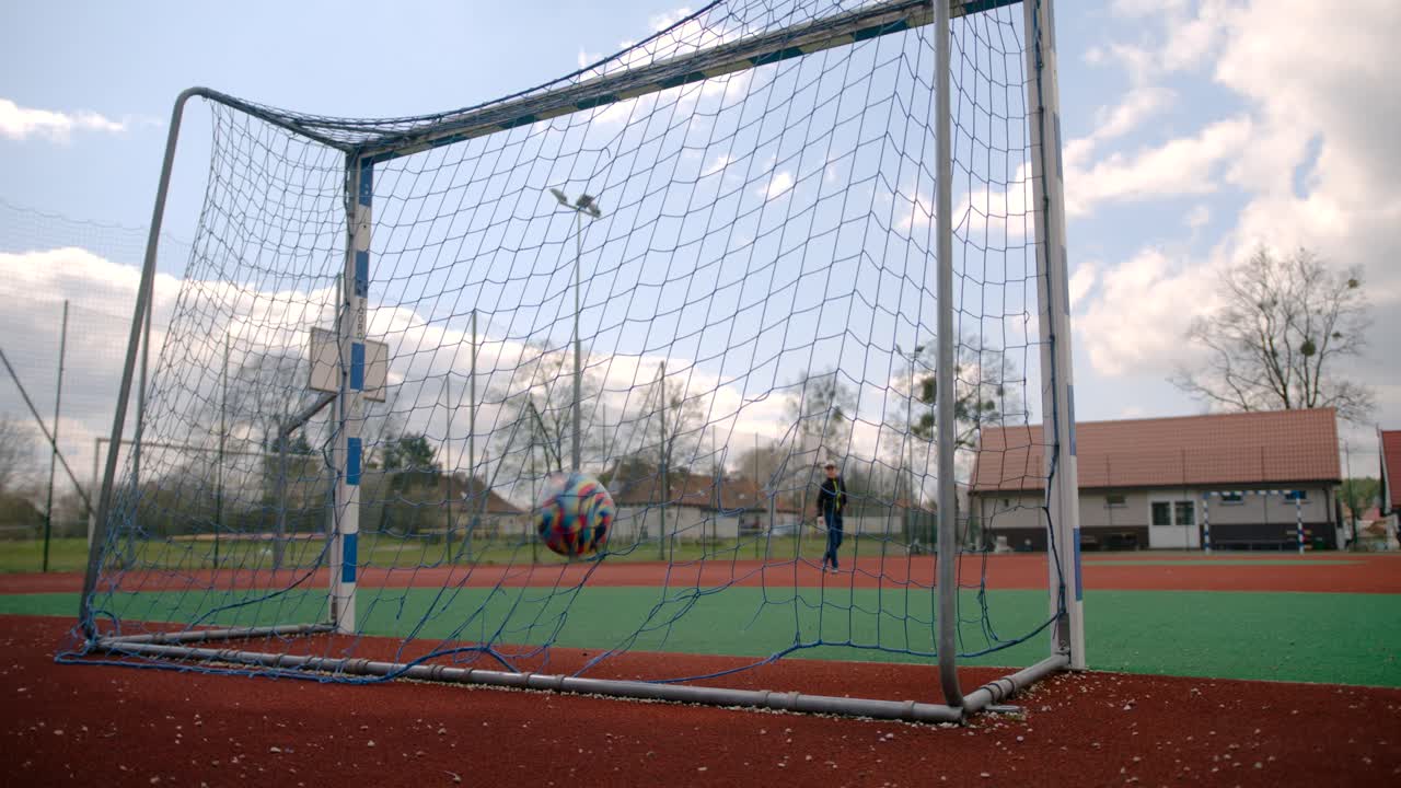 The boy shoots a free kick and scores a goal on the school field