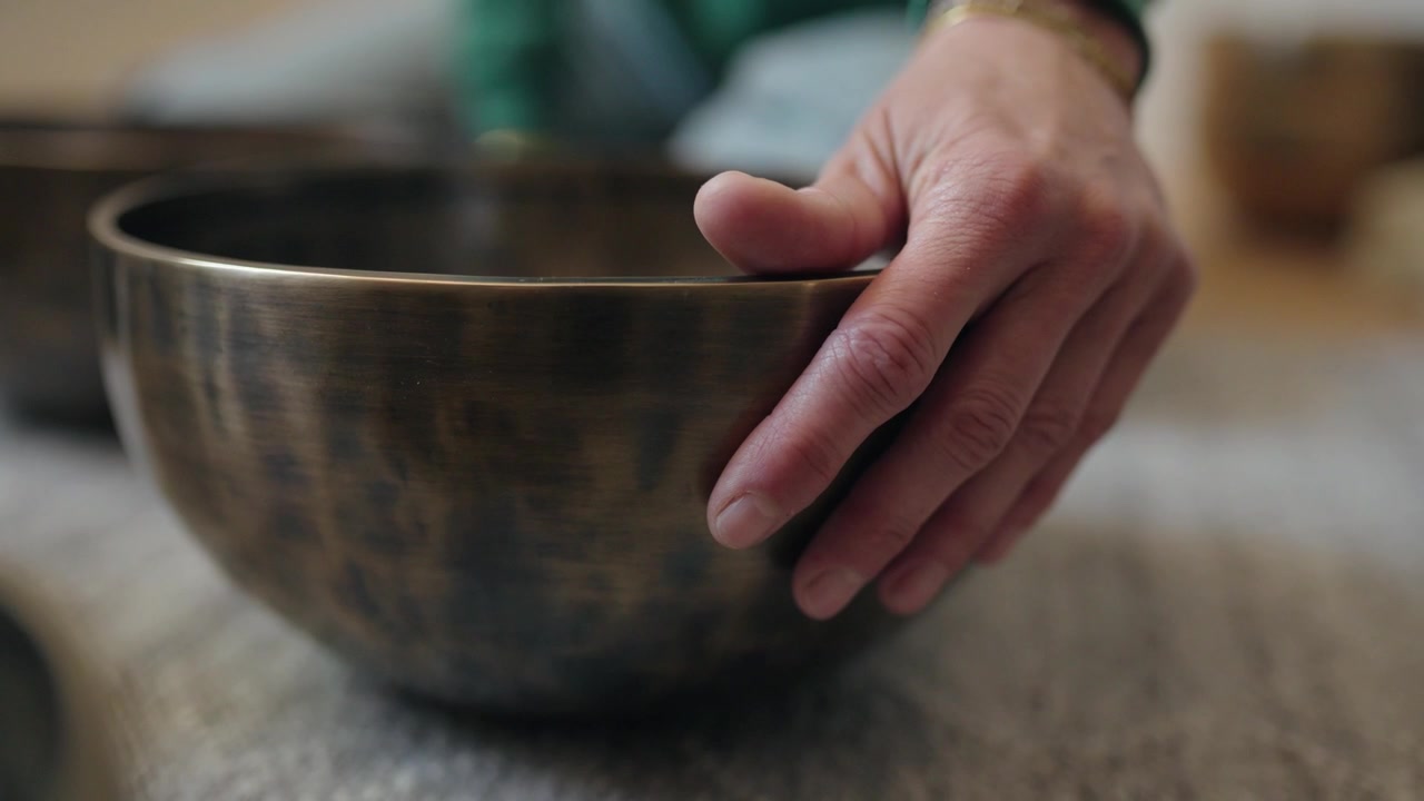 Una mano descansa suavemente sobre un cuenco tibetano vibrante para calmar su sonido.