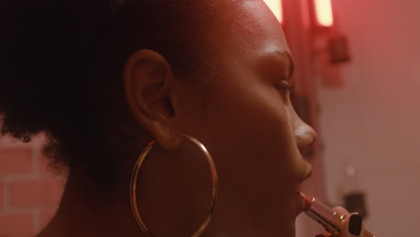 close up of a beautiful girl putting lipstick on while looking at mirror in a bar bathroom