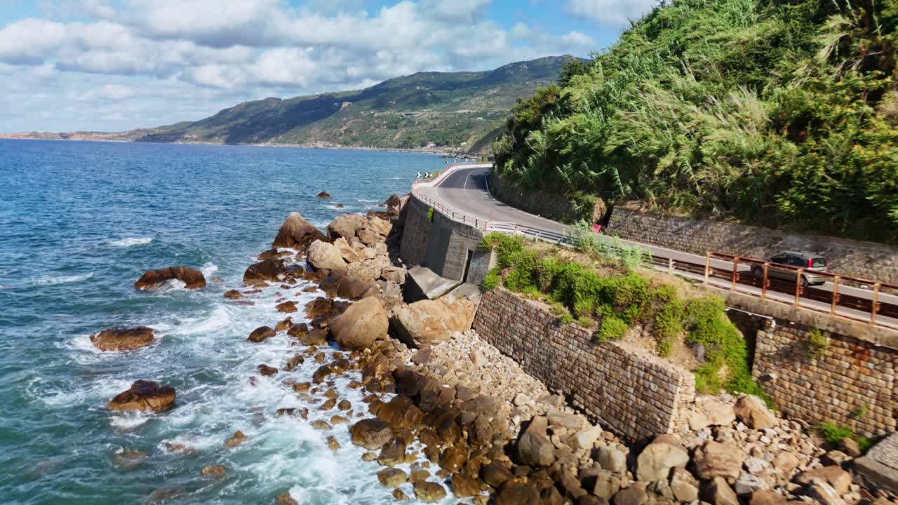 Coastal road along a blue ocean with waves hitting rocky shore