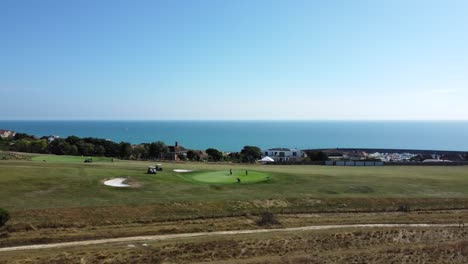 Órbita-Aérea-De-Los-Golfistas-En-El-Campo-De-Golf-Con-El-Telón-De-Fondo-Del-Océano-En-Brighton,-Reino-Unido