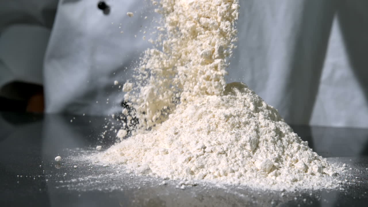 Chef sprinkling flour on black surface