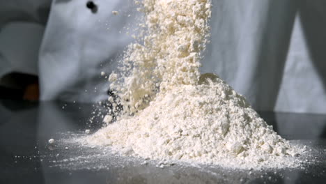 chef sprinkling flour on black surface