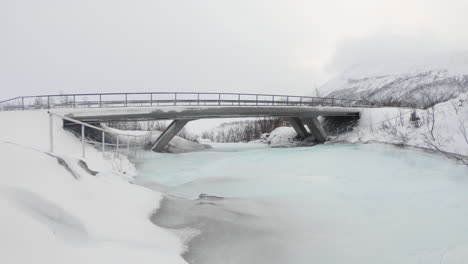 puente sobre un río congelado cerca de una cascada en björkliden, suecia