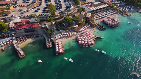 a crowded beach in ksamil, albania, with clear waters and sunbathers on wooden piers, aerial view