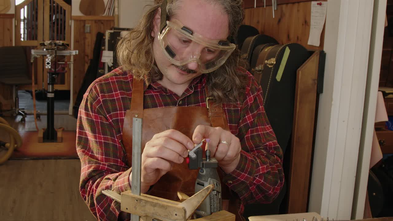 Luthier in workshop shapes new frets for guitar with electric grinder