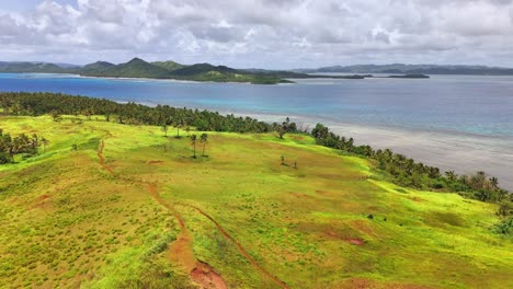 aerial shot of corregidor island, siargao, philippines with cogon grass hills, coconut palms, and views of the pacific ocean and surrounding bays in a lush tropical coastal landscape