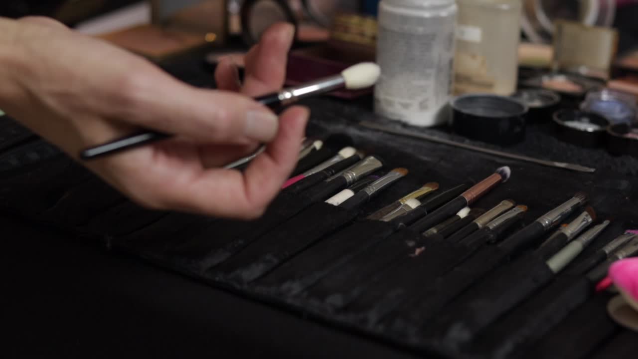 Closeup of a makeup artist's hand casually picking a makeup brush from a set